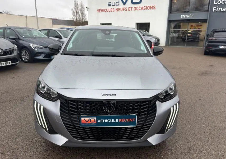 Vue avant d'une Peugeot 208 gris métallisé 2025 avec feux diurnes LED en forme de griffes et calandre noire distinctive.