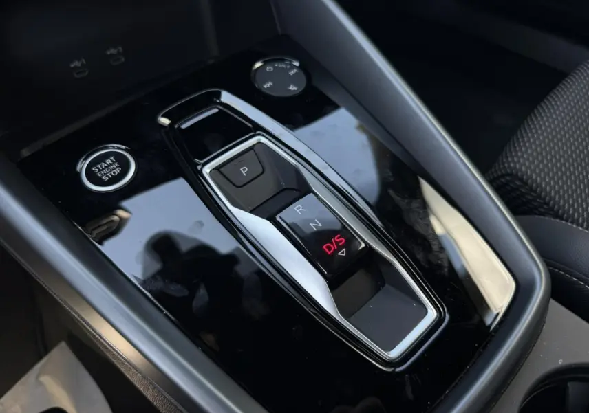 Gros plan sur la console centrale noire brillante de l'Audi A3 Sportback 2025 avec levier de vitesses automatique et bouton start/stop.