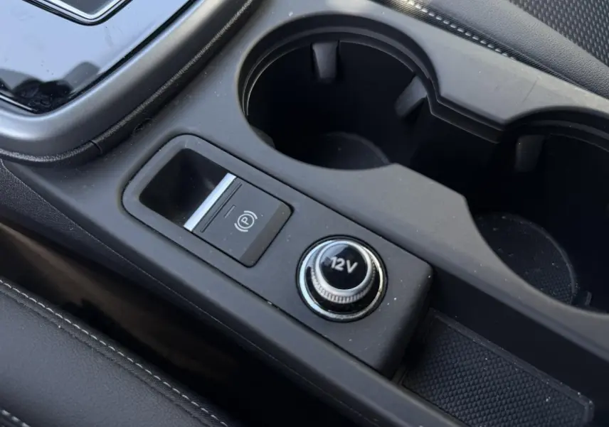 Gros plan sur la console centrale noire avec prise 12V et bouton de frein à main électrique dans une Audi A3 Sportback.