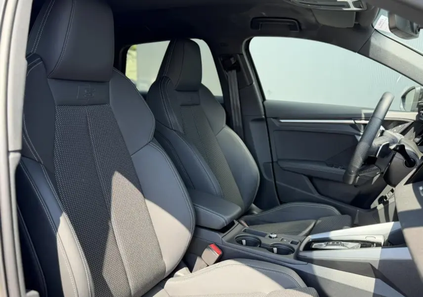Vue intérieure côté gauche de l’Audi A3 Sportback 2025 avec sièges sport noirs et volant cuir multifonctions.