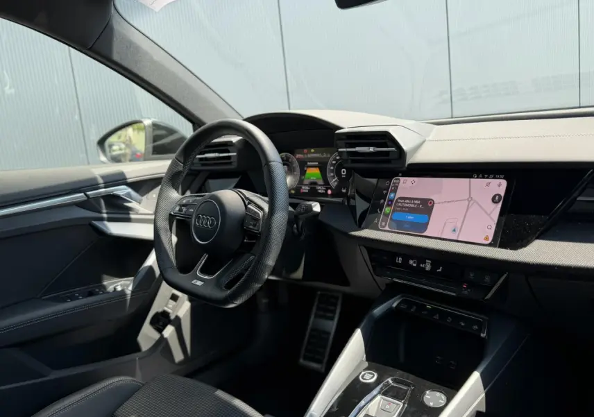 Vue intérieure côté conducteur de l'Audi A3 Sportback 2025, tableau de bord noir avec écran tactile de navigation.