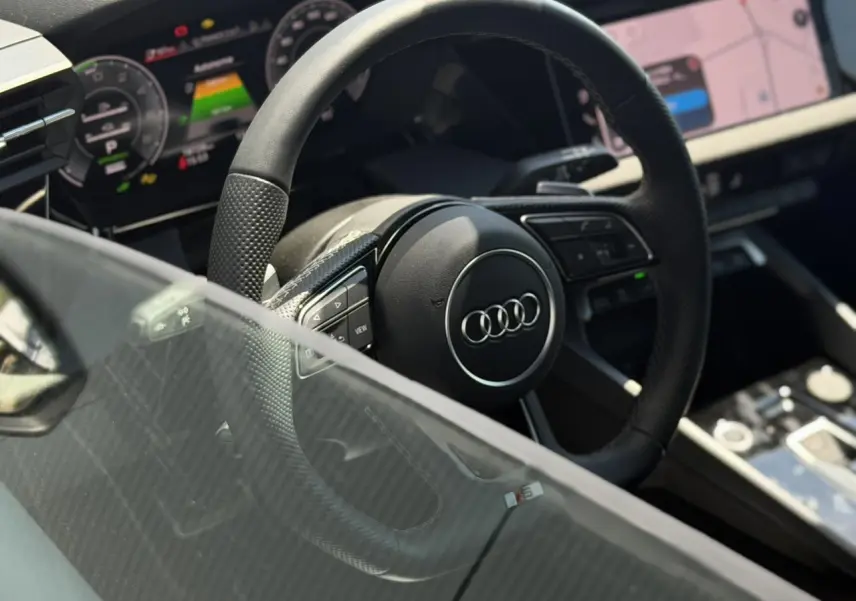 Vue intérieure centrée sur le volant cuir perforé et le tableau de bord numérique de l'Audi A3 Sportback noir Mythe.
