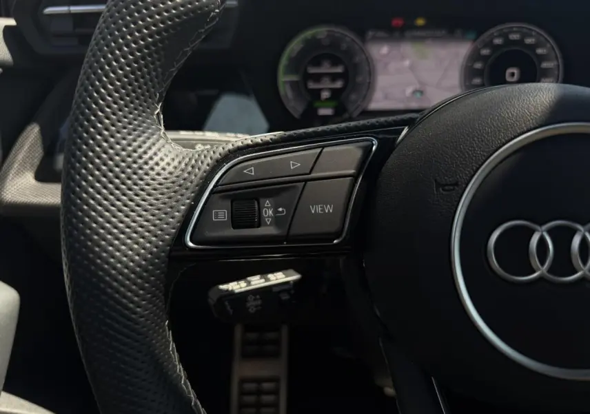 Gros plan sur le volant en cuir perforé noir de l'Audi A3 Sportback 2025 avec commandes multifonctions et tableau de bord numérique.