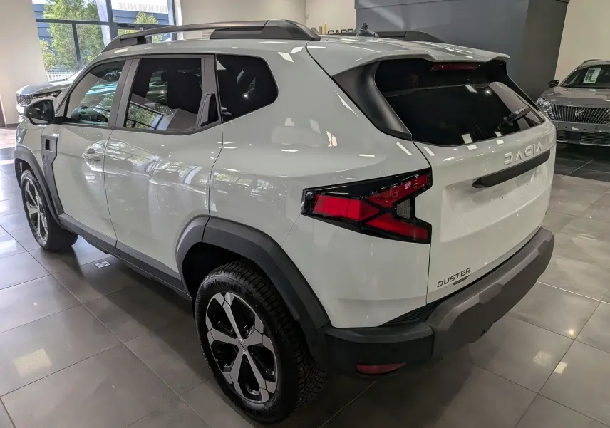 Vue 3/4 arrière droite du Dacia Duster blanc Glacier, soulignant ses feux arrière au design anguleux et ses jantes bi-ton.