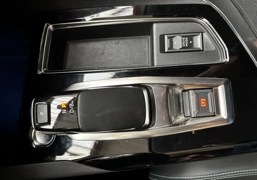 Gros plan sur la console centrale noire brillante du Peugeot 3008 hybride avec levier de vitesses et bouton frein électrique allumé.