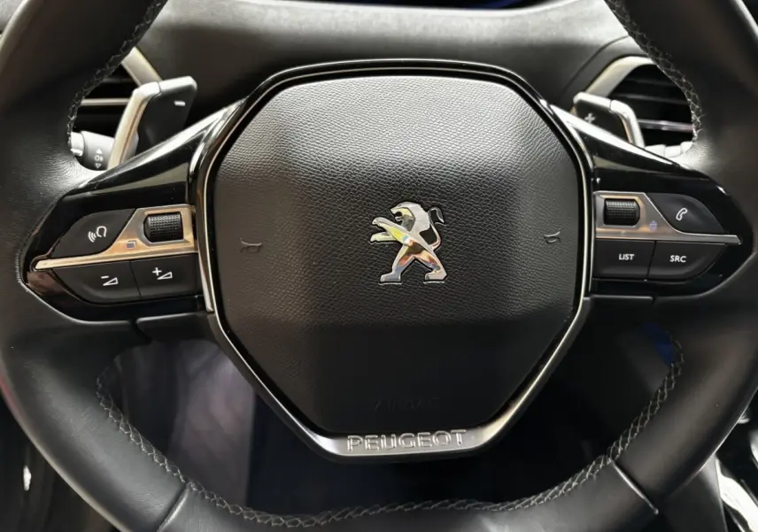 Gros plan sur le volant cuir noir du Peugeot 3008 1.6 HYBRID 225 Allure Pack avec commandes intégrées et logo lion chromé.