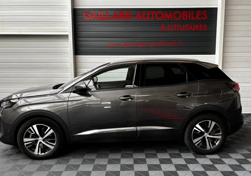 Profil côté gauche d'un Peugeot 3008 gris foncé hybride rechargeable, avec jantes alliage et vitres teintées, en intérieur showroom.