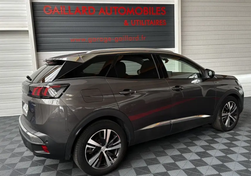 Vue 3/4 arrière droite d'un Peugeot 3008 gris foncé hybride rechargeable dans un garage avec sol damier.