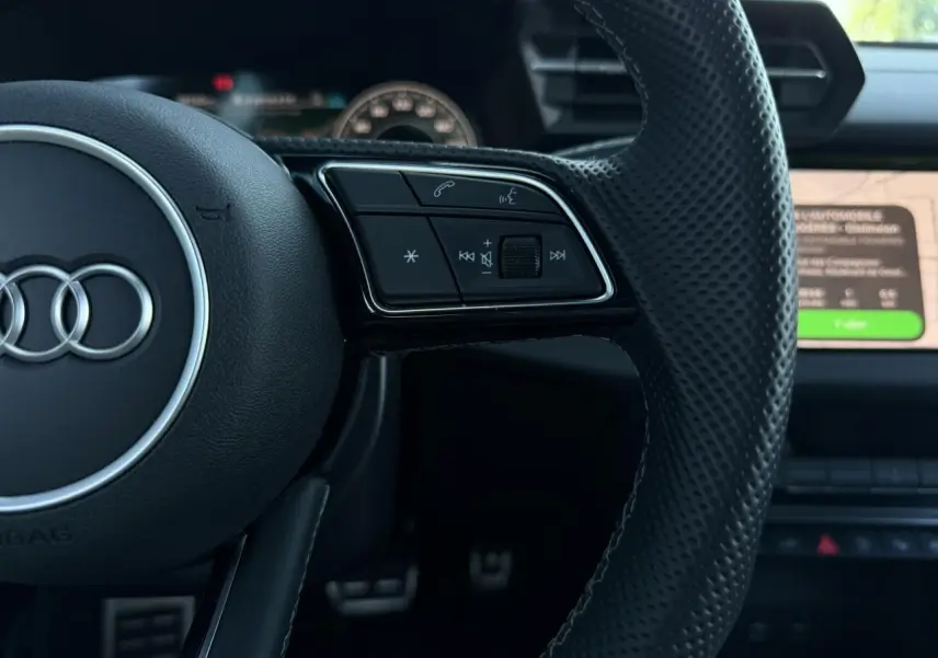 Gros plan sur le volant en cuir perforé noir de l'Audi A3 Sportback 2025 avec commandes multifonctions visibles.
