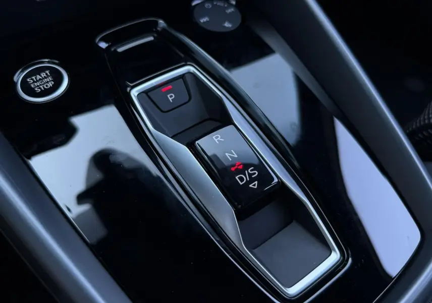 Gros plan sur la console centrale noire brillante avec sélecteur de boîte automatique et bouton Start/Stop d'une Audi A3 Sportback blanche.