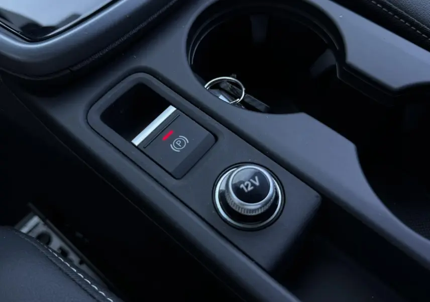 Gros plan sur la console centrale noire de l'Audi A3 Sportback 2025, avec bouton frein à main électronique et prise 12V.