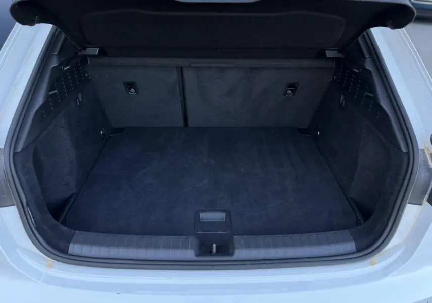 Coffre ouvert vu de l'arrière d'une Audi A3 Sportback blanc glacier, intérieur du coffre en tissu noir.