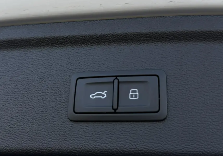 Boutons de commande pour hayon électrique et verrouillage, intégrés dans le panneau intérieur noir du coffre d'une Audi A3 Sportback blanche.