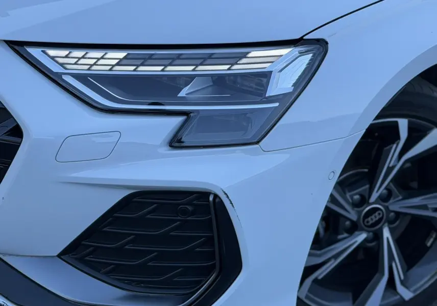 Gros plan sur l'avant droit blanc Glacier d'une Audi A3 Sportback 2025 avec phares Matrix LED et jante alliage 5 branches en Y.