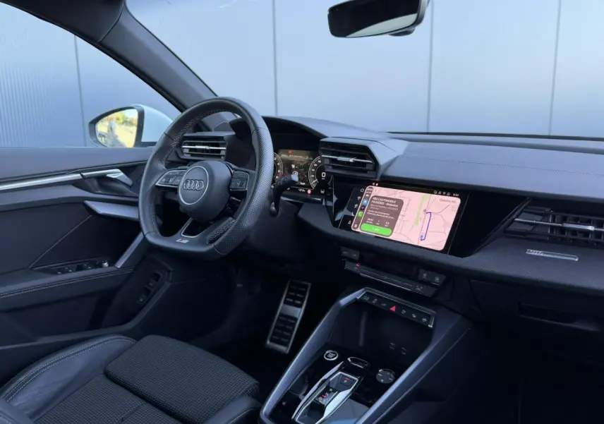 Vue intérieure côté conducteur de l'Audi A3 Sportback 2025, tableau de bord noir avec écran tactile de navigation allumé.