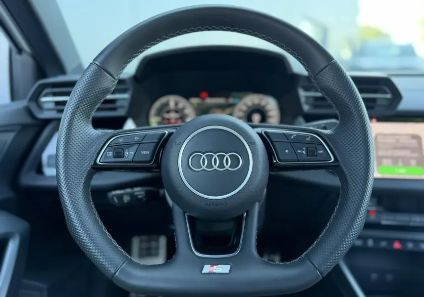 Volant sport en cuir perforé avec logo S Audi, vue frontale du poste de conduite intérieur noir.