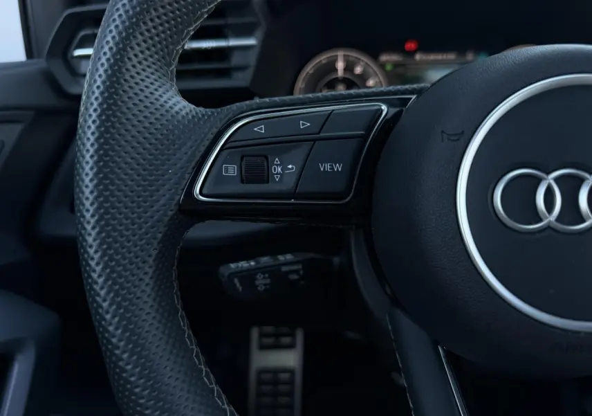 Gros plan sur le volant cuir perforé noir de l'Audi A3 Sportback 2025 avec commandes multifonctions et logo Audi central.