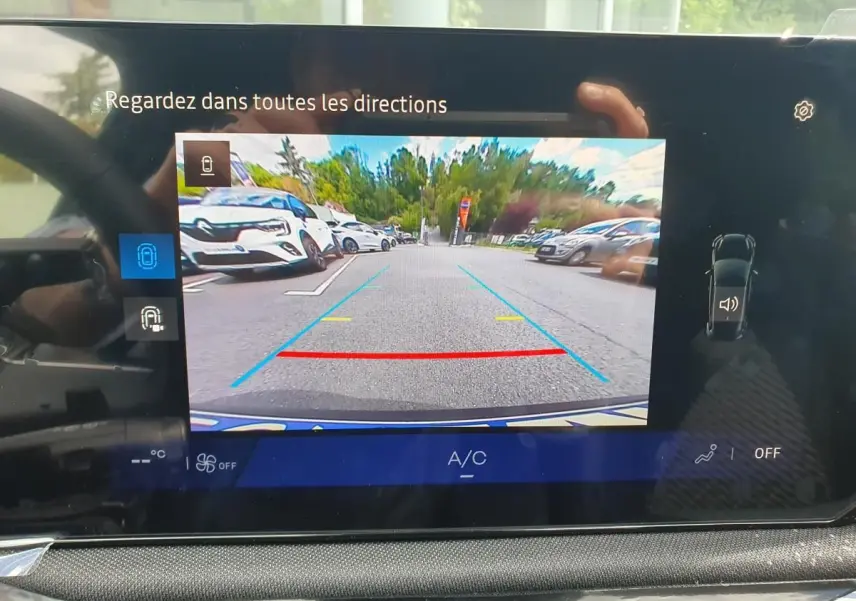 Écran multimédia de Renault Clio VI montrant la caméra de recul avec vue arrière dégagée sur parking extérieur.
