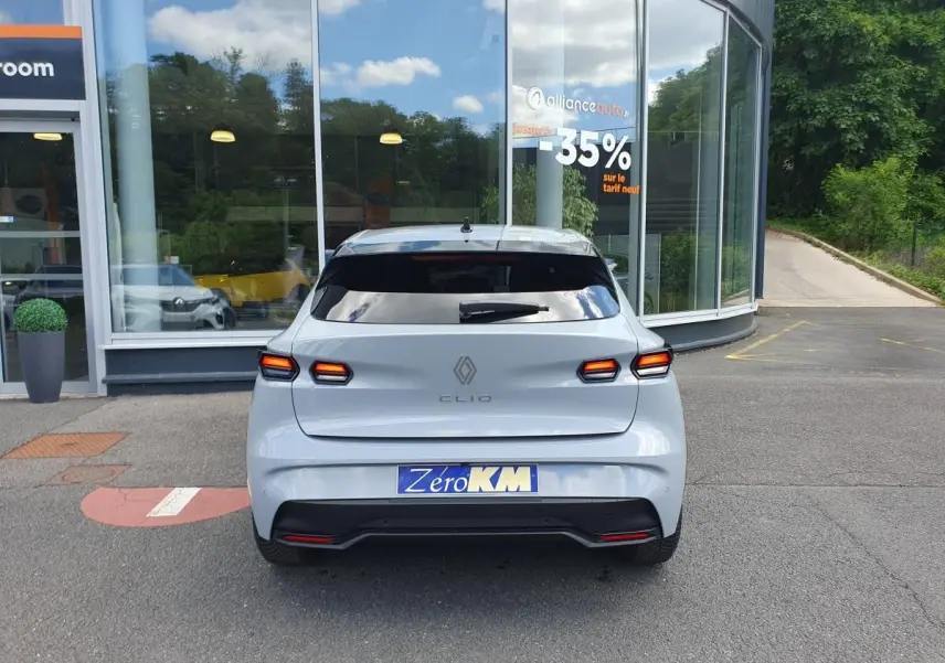Vue arrière d'une Renault Clio VI gris Rafale avec feux LED et lunette arrière surteintée, stationnée devant une vitrine.