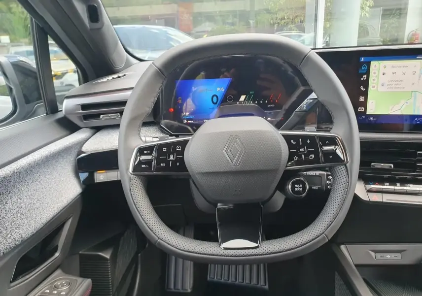 Vue intérieure centrée sur le volant multifonction de la Renault Clio VI avec tableau de bord numérique et écran tactile.