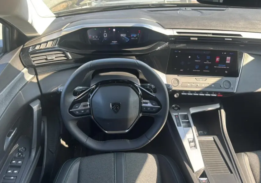 Vue intérieure du poste de conduite de la Peugeot 308 2025, volant multifonction et écran tactile central visibles.