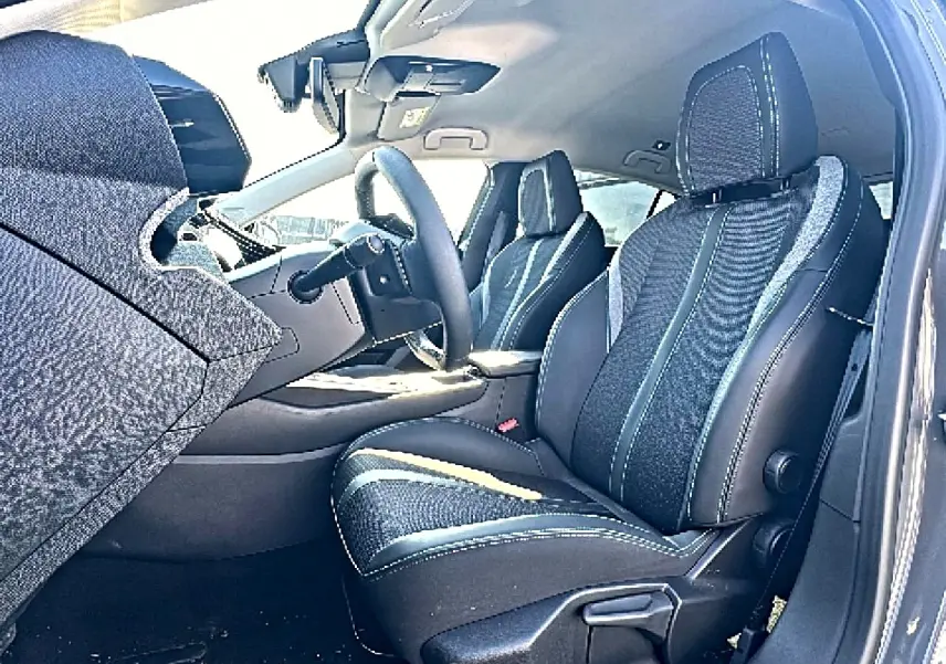 Vue intérieure côté conducteur de la Peugeot 308 2025, sièges tissu noir avec surpiqûres contrastantes et volant multifonction.