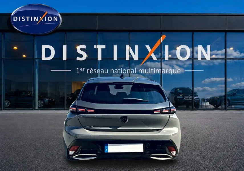 Vue arrière d'une Peugeot 308 gris selenium 2025 garée devant une vitrine avec logo Distinxion.