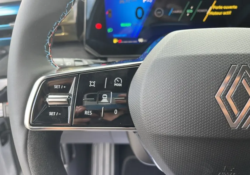 Gros plan sur le volant multifonctions de la Renault Clio 6 E-Tech 160 Esprit Alpine avec commandes de régulateur et logo central.