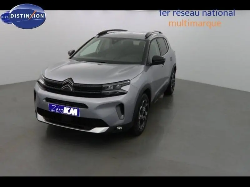 Citroën C5 Aircross gris acier vu en 3/4 avant droit, avec barres de toit et jantes alu distinctives.