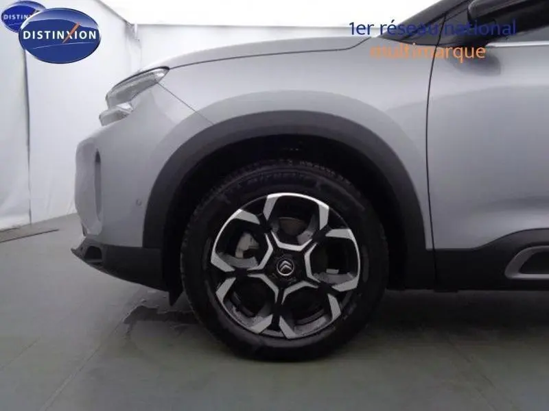 Gros plan sur la roue avant gauche d'un Citroën C5 Aircross gris acier avec jante alu au design hexagonal distinctif.