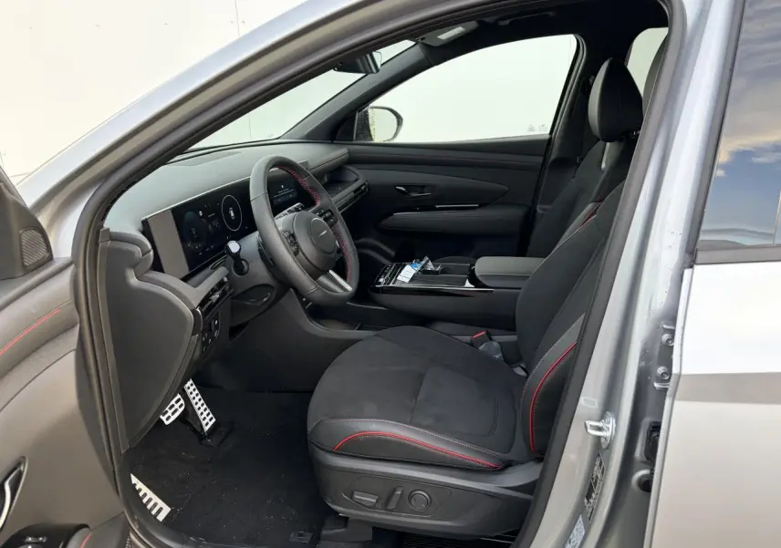 Vue intérieure côté conducteur du Hyundai Tucson 2025 argent, sièges cuir/alcantara noirs avec surpiqûres rouges et volant sport N Line.