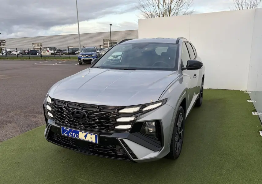 Vue 3/4 avant d'un Hyundai Tucson 2025 gris argent métallisé avec calandre noire et jantes alliage sombres.
