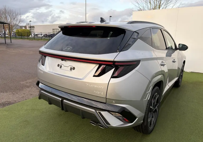 Vue 3/4 arrière droite du Hyundai Tucson 2025 hybride en argent métallisé avec feux arrière à bandeau lumineux et double sortie d'échappement.