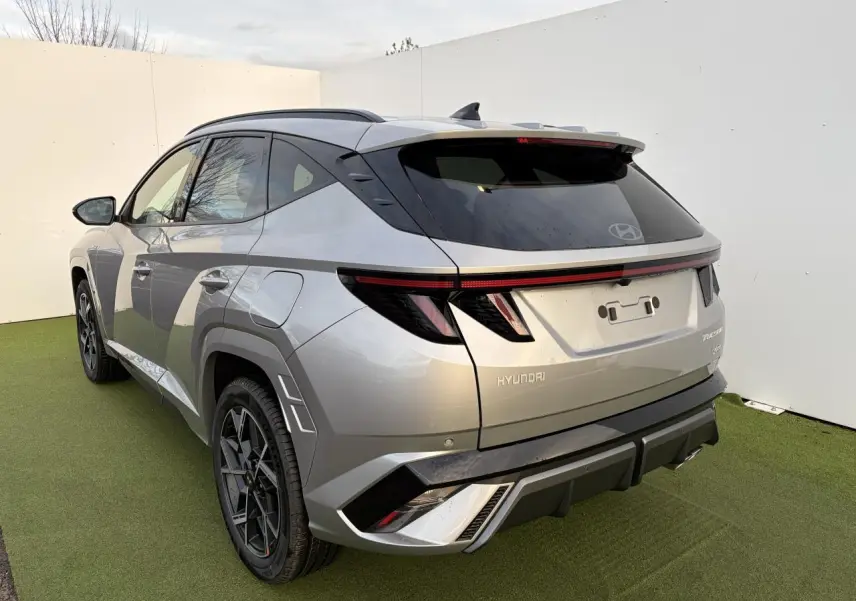 Vue 3/4 arrière gauche du Hyundai Tucson 2025 en gris métallisé avec feux arrière à LED et jantes alliage noires.