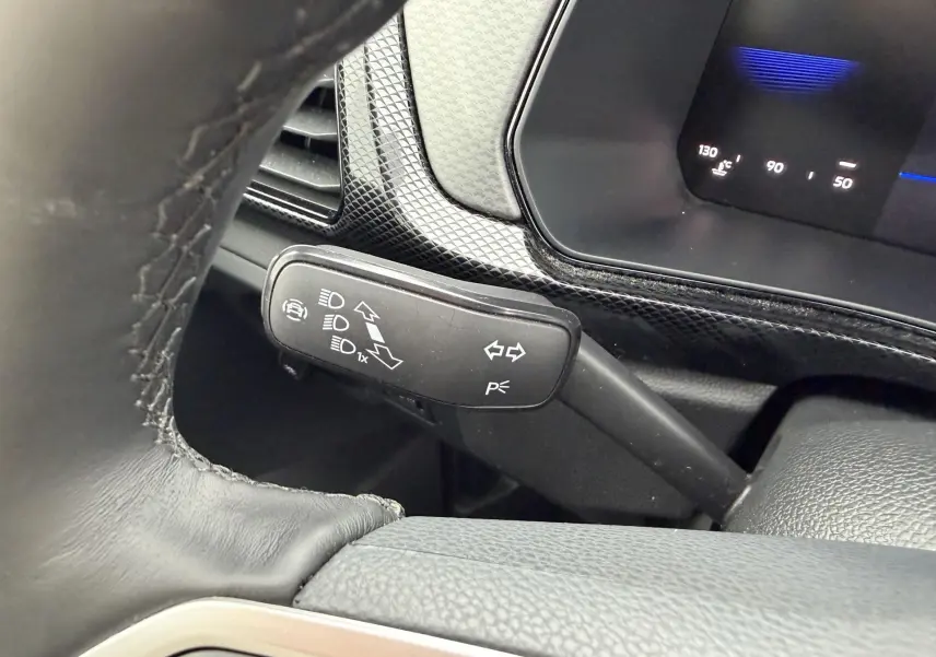 Gros plan sur la manette de clignotants et feux du Volkswagen T-Cross 2025, intérieur noir avec tableau de bord digital.