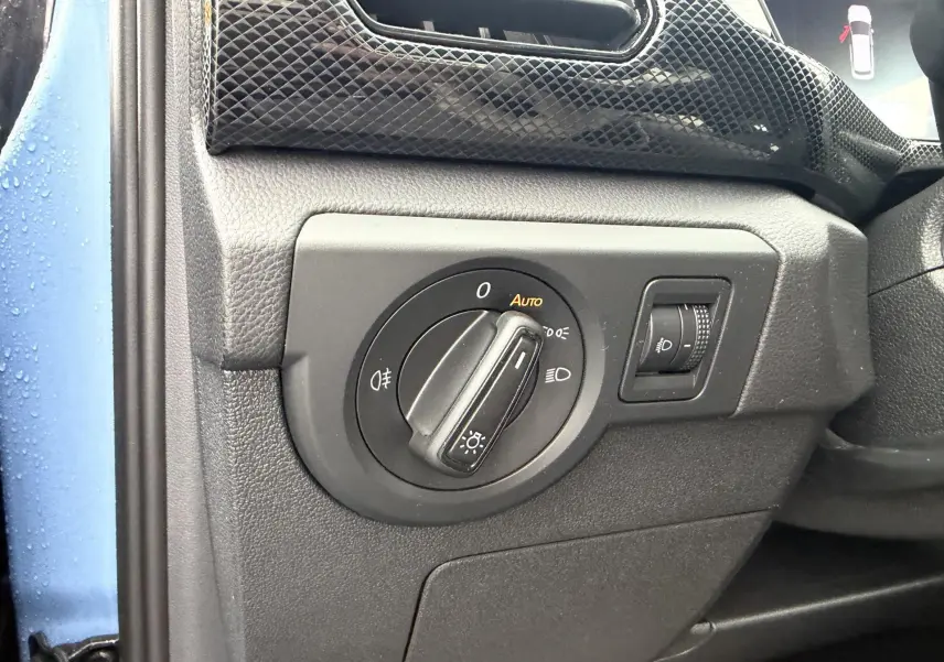 Détail du bouton de commande des phares sur le tableau de bord côté conducteur d’un Volkswagen T-Cross bleu 2025.