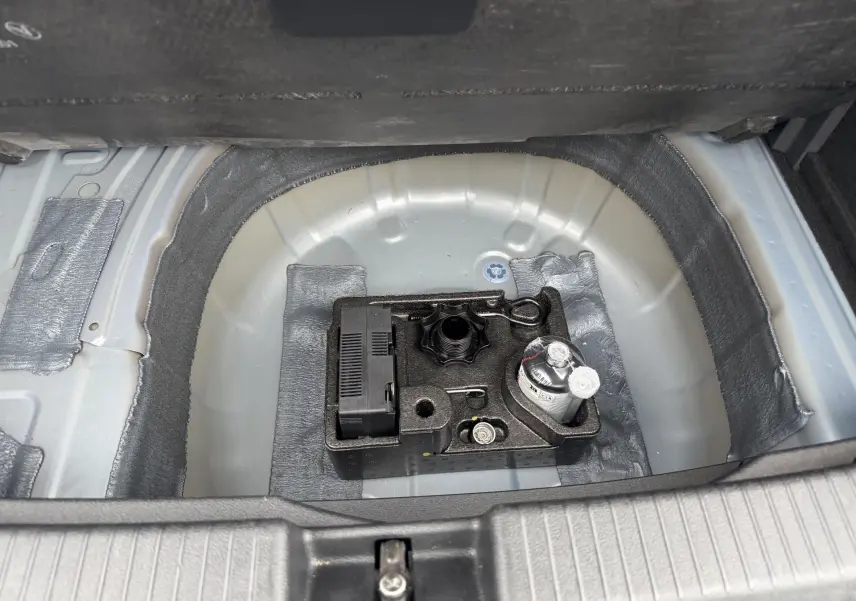 Vue plongeante sur le coffre ouvert d'un Volkswagen T-Cross 2025, montrant le rangement sous plancher avec kit de réparation pneus.