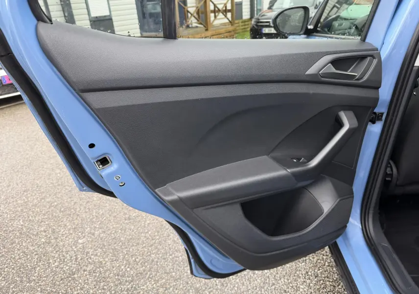 Vue rapprochée de la porte arrière gauche bleu clair du Volkswagen T-Cross 2025 avec poignée et bouton de lève-vitre.