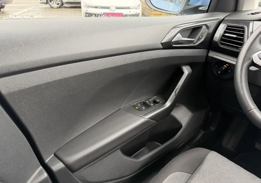Vue intérieure côté conducteur du Volkswagen T-Cross 2025, montrant la portière noire avec commandes des vitres et rétroviseurs.