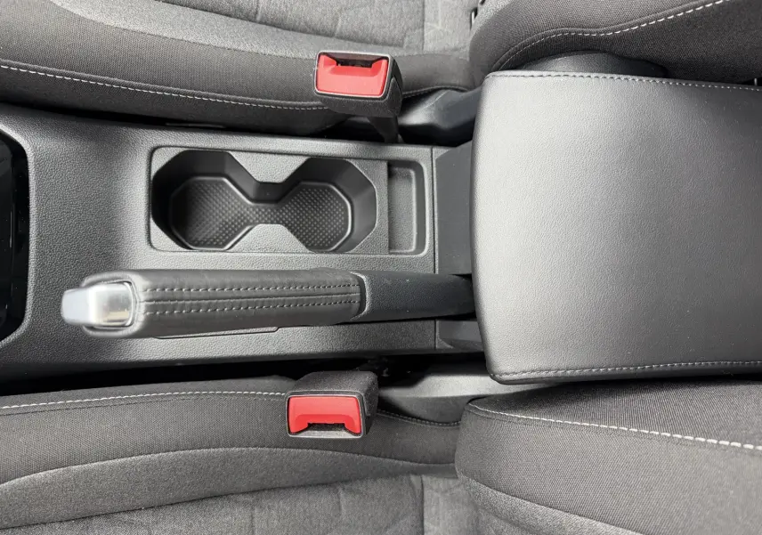 Vue plongeante sur la console centrale noire du Volkswagen T-Cross avec frein à main manuel et accoudoir cuir.