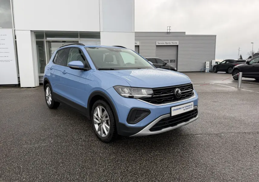 Volkswagen T-Cross bleu en 3/4 avant droit, avec jantes alliage et calandre noire brillante sous la pluie.