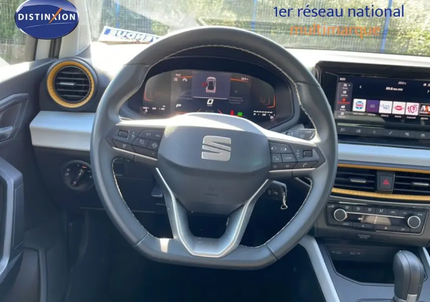 Vue intérieure centrée sur le volant et tableau de bord du SEAT Arona blanc métal avec détails noirs et écran digital.