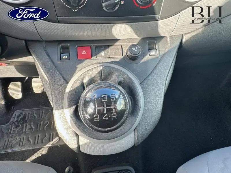 Gros plan sur le levier de vitesses manuel noir et la console centrale d’un véhicule, avec pédales visibles en arrière-plan.