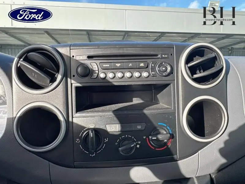 Vue rapprochée du tableau de bord noir du Peugeot Partner Tepee blanc, montrant la console centrale avec commandes de climatisation et autoradio.