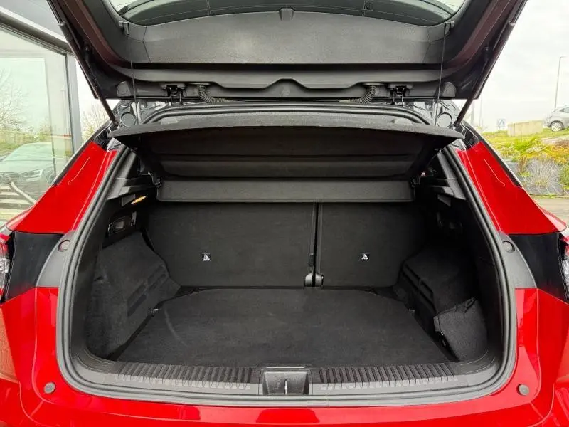 Coffre ouvert vu de l'arrière d'un Renault Austral 2025 rouge flamme, montrant l'espace de chargement vide et la trappe de séparation.