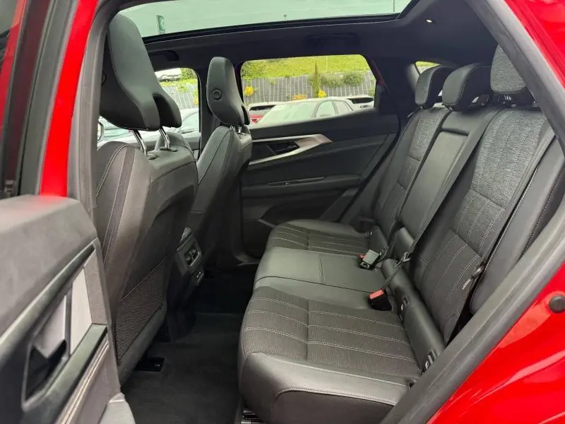 Vue intérieure arrière gauche du Renault Austral 2025 rouge Flamme, montrant les sièges arrière en tissu noir avec surpiqûres.