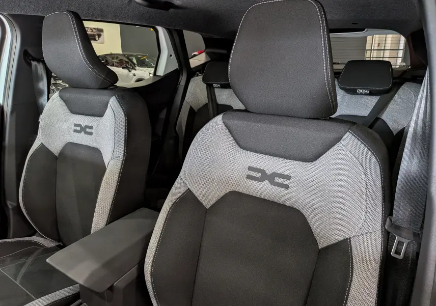 Vue intérieure rapprochée des sièges avant gris et noirs du Dacia Duster Hybrid-G 150 CH 4x4 Journey avec logo distinctif brodé.
