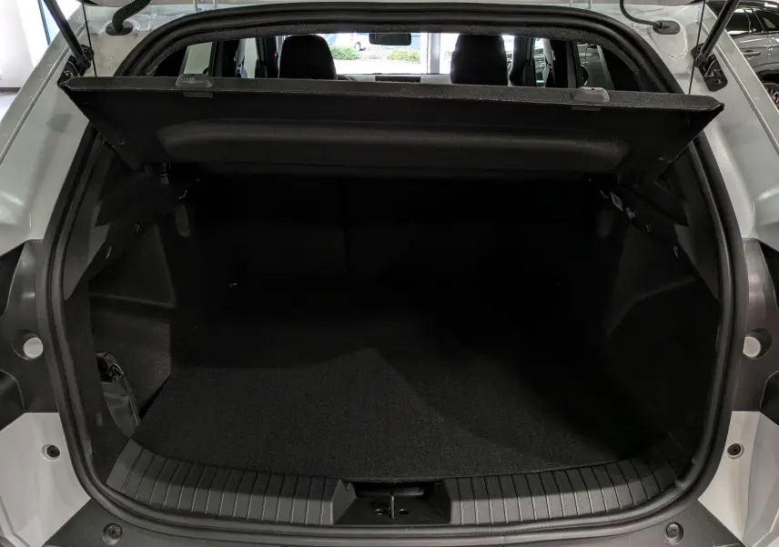 Coffre ouvert vu de l'arrière d'un Dacia Duster Hybrid-G blanc Glacier, montrant l'espace de chargement et la tablette arrière.
