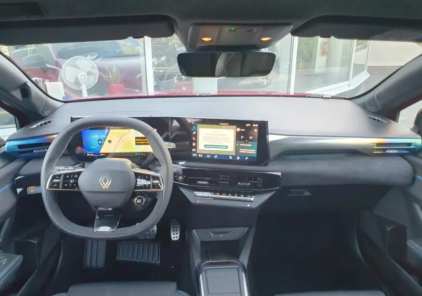Vue intérieure avant de la Renault Clio VI hybride rouge, tableau de bord moderne avec double écran tactile et volant multifonction.