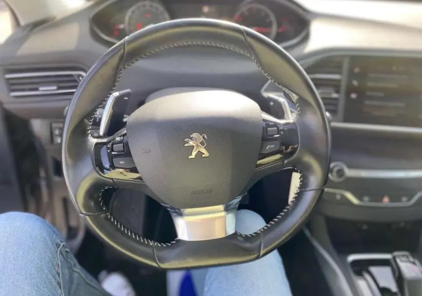 Vue centrée sur le volant cuir noir du Peugeot 308 SW 2019, avec tableau de bord et console en arrière-plan flouté.